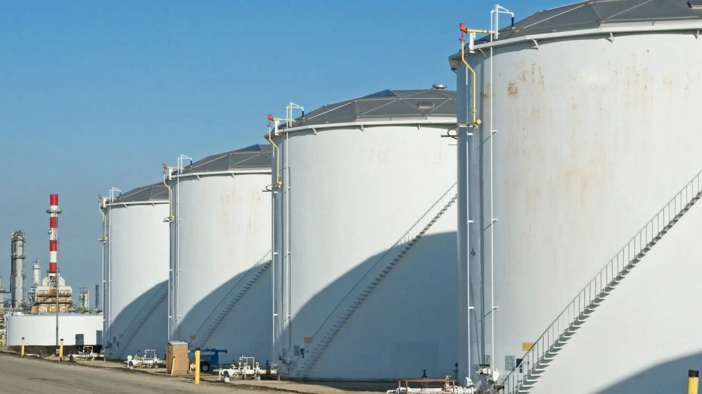 A row of white bulk petroleum storage tanks with access stairways at a fuel terminal